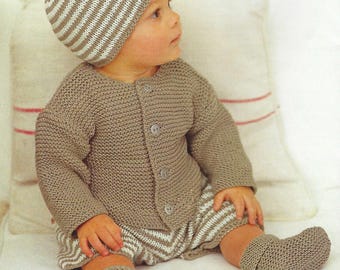 May include: A knitted baby outfit in a soft, neutral color. The set includes a button-up cardigan, shorts, a striped beanie, and booties. The shorts and beanie feature a striped pattern. The outfit is designed for comfort and warmth.
