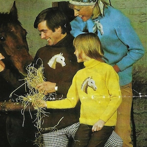 May include: A family of three wearing jumpers with horse designs. The jumpers are brown, blue, and yellow. The family are standing in front of a brown horse.