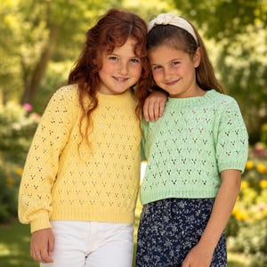 Può includere: Due giovani con maglioni di maglia. Uno è giallo, l'altro verde chiaro. Entrambi i maglioni hanno un delicato motivo traforato. La persona a sinistra indossa pantaloni bianchi, e quella a destra una gonna con fantasia floreale.