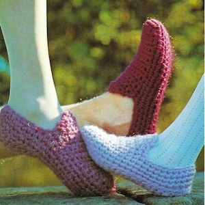 May include: Two pairs of crocheted slippers, one in purple and one in light blue. The slippers are being worn on the feet of two people.