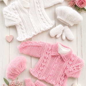 Puede incluir: Un conjunto de dos cárdigans de punto para bebé, uno blanco y otro rosa. Cada conjunto incluye un cárdigan de manga larga con botones, detalles texturizados de trenzas y pompones, una boina a juego y un par de manoplas de punto pequeñas.