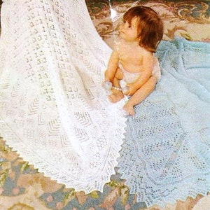 May include: Two white crocheted baby blankets with a delicate lace pattern. One blanket is draped over a baby sitting on a patterned rug.