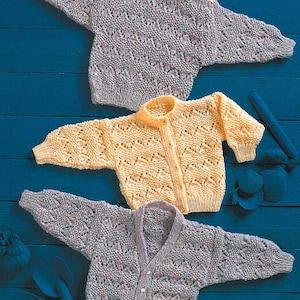 May include: Three knitted baby cardigans in different colours: purple, yellow, and light blue. The cardigans have a lacy pattern and button fastenings.
