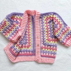May include: A crocheted cardigan in shades of pink, purple and yellow. The cardigan has a button fastening and long sleeves.
