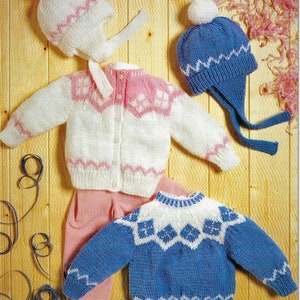 Peut inclure: Deux pulls en tricot pour bébé avec des bonnets assortis. Un pull est blanc avec des motifs de flocons de neige roses et l'autre est bleu avec des motifs de flocons de neige blancs. Les deux bonnets ont des pompons blancs.