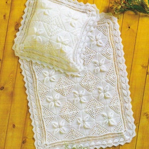 May include: A white crocheted baby blanket with a matching pillow. The blanket features a delicate floral pattern and a scalloped border.