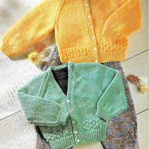 May include: Two knitted cardigans, one yellow and one green, with button closures. Both cardigans have a textured stitch pattern and are laid out on a patterned fabric.
