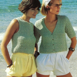 May include: Two women wearing knitted tops and shorts. The woman on the left is wearing a sleeveless green top and yellow shorts. The woman on the right is wearing a green cardigan with a button closure and white shorts.