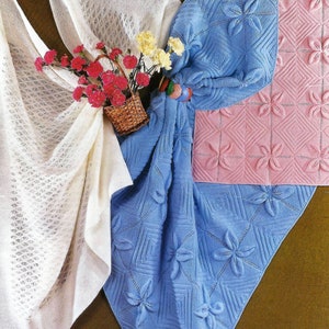 Puede incluir: Tres mantas de bebé de punto en blanco, rosa y azul. Las mantas están hechas con un delicado patrón de punto y presentan un diseño floral.