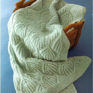 May include: A soft, green knitted blanket with a leaf pattern. The blanket is folded and placed in a wooden basket.