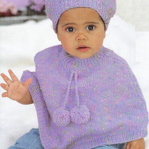 Könnte beinhalten: Ein lila gestricktes Poncho mit Bommeln an den Bändern und einer passenden lila gestrickten Baskenmütze. Das Poncho hat ein gesprenkeltes Muster mit mehrfarbigen Flecken.
