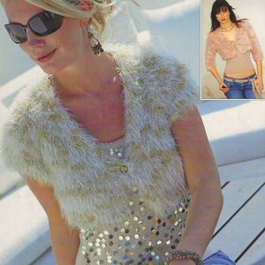 May include: A white and gold fuzzy knit shrug with a button closure. The shrug is worn over a sequined top and blue jeans.