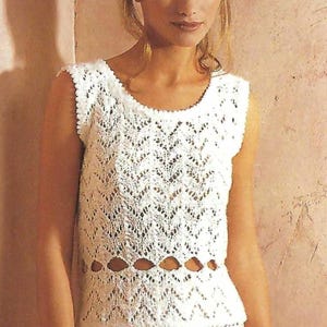 May include: A sleeveless white crochet top with a scalloped neckline and a row of oval cutouts. The top is paired with a matching white skirt. The crochet pattern features a delicate openwork design, creating a textured and airy look. The outfit is suitable for warm weather.