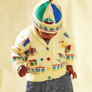 Może przedstawiać: Biały dzianinowy kardigan z kolorowym wzorem zwierząt i zabawek. Kardigan zapinany na guziki, z kołnierzem. Dziecko ma na sobie również białą i niebieską dzianinową czapkę z kolorowym wzorem.