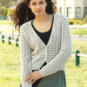 May include: A white crocheted cardigan with a V-neck and button fastening. The cardigan features a delicate openwork pattern and is worn over a black vest top.