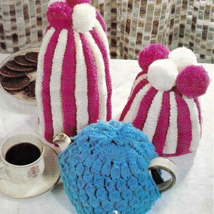 Könnte beinhalten: Drei gestrickte Teekannen-Überzüge. Zwei sind rosa und weiß gestreift mit weißen Bommeln. Einer ist blau mit einem strukturierten Design.
