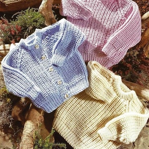 May include: Three knitted baby cardigans in different colours: light blue, pink and cream. The cardigans have a simple design with a button fastening.