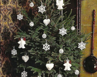 Puede incluir: Un árbol de Navidad blanco decorado con adornos de ganchillo, incluyendo ángeles, estrellas, corazones y copos de nieve. El árbol está decorado con adornos blancos y está delante de una chimenea.