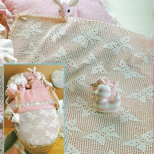 May include: A white crocheted baby blanket with a delicate pattern. The blanket is draped over a pink pillow and a wicker basket with a pink lining. There are stuffed animals in the basket, including a bunny and a duck.