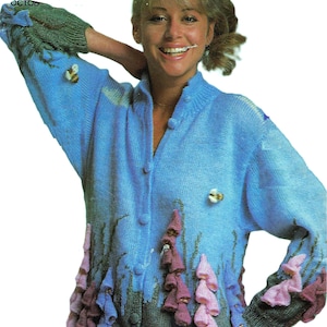 Puede incluir: Un cárdigan azul de punto con un diseño floral. El cárdigan tiene un cierre de botones en la parte delantera y mangas largas. El diseño floral presenta flores rosas, moradas y verdes.