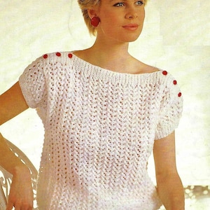 Peut inclure: Top en crochet blanc avec un col bateau et des manches courtes. Le haut a des boutons rouges sur les épaules.