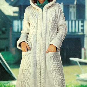 May include: A white knitted hooded cardigan with a cable knit pattern and a zip closure. The cardigan has pockets on the front and is made with a textured yarn.