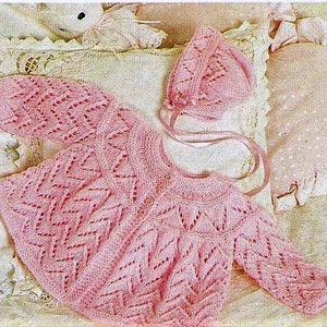 May include: A pink knitted baby cardigan and matching hat with a delicate lace pattern.