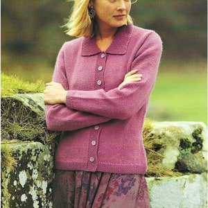 May include: A woman wearing a pink knitted cardigan with a collared neckline and button closure. She is standing in front of a stone wall and wearing a floral skirt.