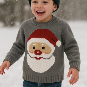 May include: A child wearing a gray sweater with a Santa Claus face design, a red hat, and a white beard. The child is also wearing a dark green beanie and blue jeans. The background is a snowy scene.