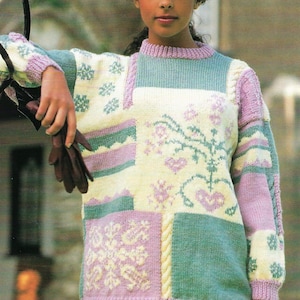 Op de afbeelding: Een vrouw draagt een veelkleurige gebreide trui met een patchwork-ontwerp. De trui heeft verschillende kleuren, waaronder roze, wit en groen. De vrouw draagt ook een bruine hoed met een veer.