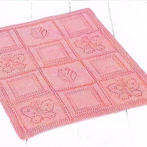 Peut inclure: Une couverture pour bébé en tricot rose avec un motif répétitif de papillons et de fleurs. La couverture est réalisée avec un point délicat et a une sensation douce et confortable.