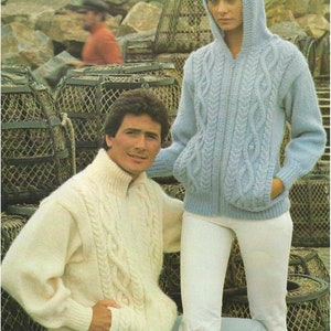 May include: Two people wearing cable knit sweaters. The person on the left is wearing a white sweater and the person on the right is wearing a light blue sweater with a hood. Both sweaters have a zipper closure.