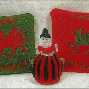 May include: Two green and red knitted cushions with a red dragon and a green dragon on them. The cushions have the text " Cymru Am Byth" on them. A red and black knitted doll is in the middle of the cushions.