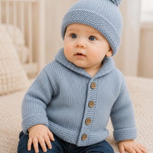 Peut inclure: Un gilet en tricot bleu clair avec un col châle et quatre boutons marron, associé à un bonnet en tricot bleu clair assorti avec un pompon sur le dessus. La tenue est portée avec un jean bleu foncé, créant un ensemble coordonné.