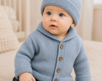 May include: A light blue knit cardigan with a shawl collar and four brown buttons, paired with a matching light blue knit beanie featuring a pom-pom on top. The outfit is worn with dark blue denim jeans, creating a coordinated look.