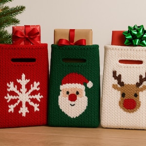 Puede incluir: Tres bolsas de regalo navideñas de punto en rojo, verde y crema. La bolsa roja tiene un copo de nieve blanco, la bolsa verde tiene a Papá Noel y la bolsa crema tiene un reno. Cada bolsa tiene un asa y contiene un regalo envuelto.