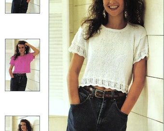 May include: A woman is wearing a white crocheted top with a scalloped hem and blue jeans. She is standing in front of a white wall with a window behind her.