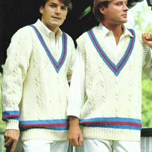 May include: Two people in cream cable-knit cricket sweaters with a V-neck. The sweaters feature blue and red stripes on the neckline, cuffs, and hem. The image includes the text: 86-112cm. (34-44ins.)