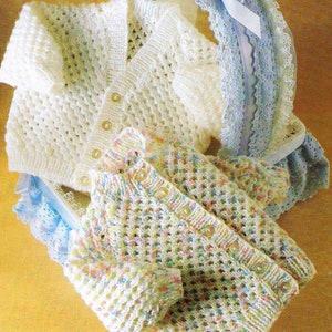 May include: Two knitted baby cardigans, one white and one with a multi-coloured pattern. The cardigans are laid out on a light brown surface with a blue and white lace trim.