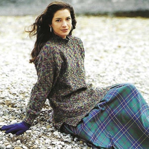 Könnte beinhalten: Eine Frau trägt einen grün-braun-violetten gemusterten Pullover mit langen Ärmeln und einem hohen Kragen. Sie trägt auch einen blau-grünen karierten Rock.