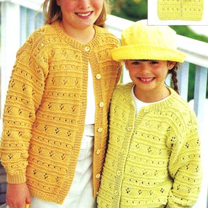 May include: Two young people wearing matching yellow knitted cardigans. The cardigans have a button-up front and a textured pattern. One person is wearing a yellow hat. The cardigans are a light yellow colour.