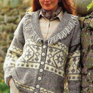 Könnte beinhalten: Eine Frau trägt einen grau-, creme- und braun gemusterten Cardigan-Pullover mit Fransenkragen. Der Pullover hat eine Knopfleiste vorne und wird mit einem Hemd mit Kragen und einem Schal kombiniert. Die Frau lehnt an einer Steinmauer.