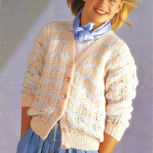 Puede incluir: Un cárdigan rosa claro con un patrón azul y blanco. El cárdigan tiene cuello en V y botones en la parte delantera. La modelo lleva pantalones vaqueros azules.