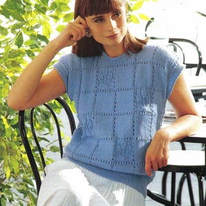 May include: A light blue knitted sleeveless top with a delicate floral pattern. The top has a round neckline and is made of a soft, lightweight yarn.