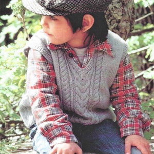 Puede incluir: Un niño con un chaleco gris de punto trenzado sobre una camisa a cuadros roja y negra, combinado con vaqueros azules. El niño también lleva una gorra gris y negra estampada. El atuendo es adecuado para el clima fresco.
