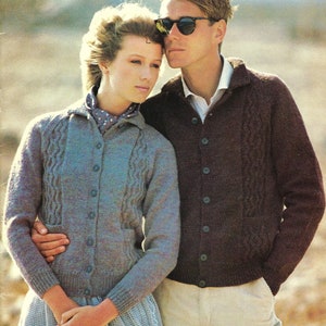 May include: A couple wearing knitted cardigans. The woman is wearing a light blue cardigan with a cable knit design and button closure. The man is wearing a brown cardigan with a similar cable knit pattern and button closure. Both cardigans have a collared neckline.