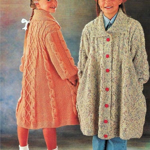 May include: Two girls in knitted coats. One is peach-coloured with a cable knit pattern, the other is speckled with red buttons. Both coats have a collared neckline and long sleeves. The coats are knee-length.