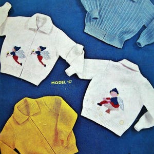 Op de afbeelding: Een verzameling gebreide kindertruien in verschillende kleuren, waaronder wit, blauw en geel. Sommige truien hebben geborduurde ontwerpen van engelen of feeën. Elke trui heeft een kraag en een ritssluiting.