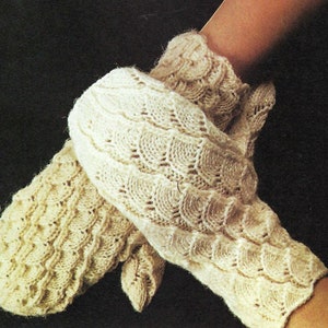 Puede incluir: Dos pares de guantes tejidos de color crema con un patrón de encaje. Los guantes están doblados juntos y sostenidos por una mano.