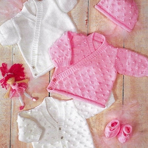 May include: Three knitted baby outfits in white and pink. The outfits include a cardigan, a wrap sweater, and a hat. The outfits are made with a textured stitch that creates a bumpy surface.
